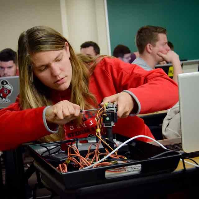 A female student in Engineering class works with a device in class.